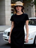 Woman wearing a black dress and beige bucket hat standing on a street.