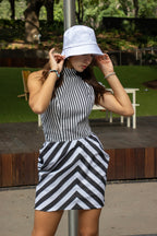 Woman wearing a black and white striped dress and white bucket hat outdoors.