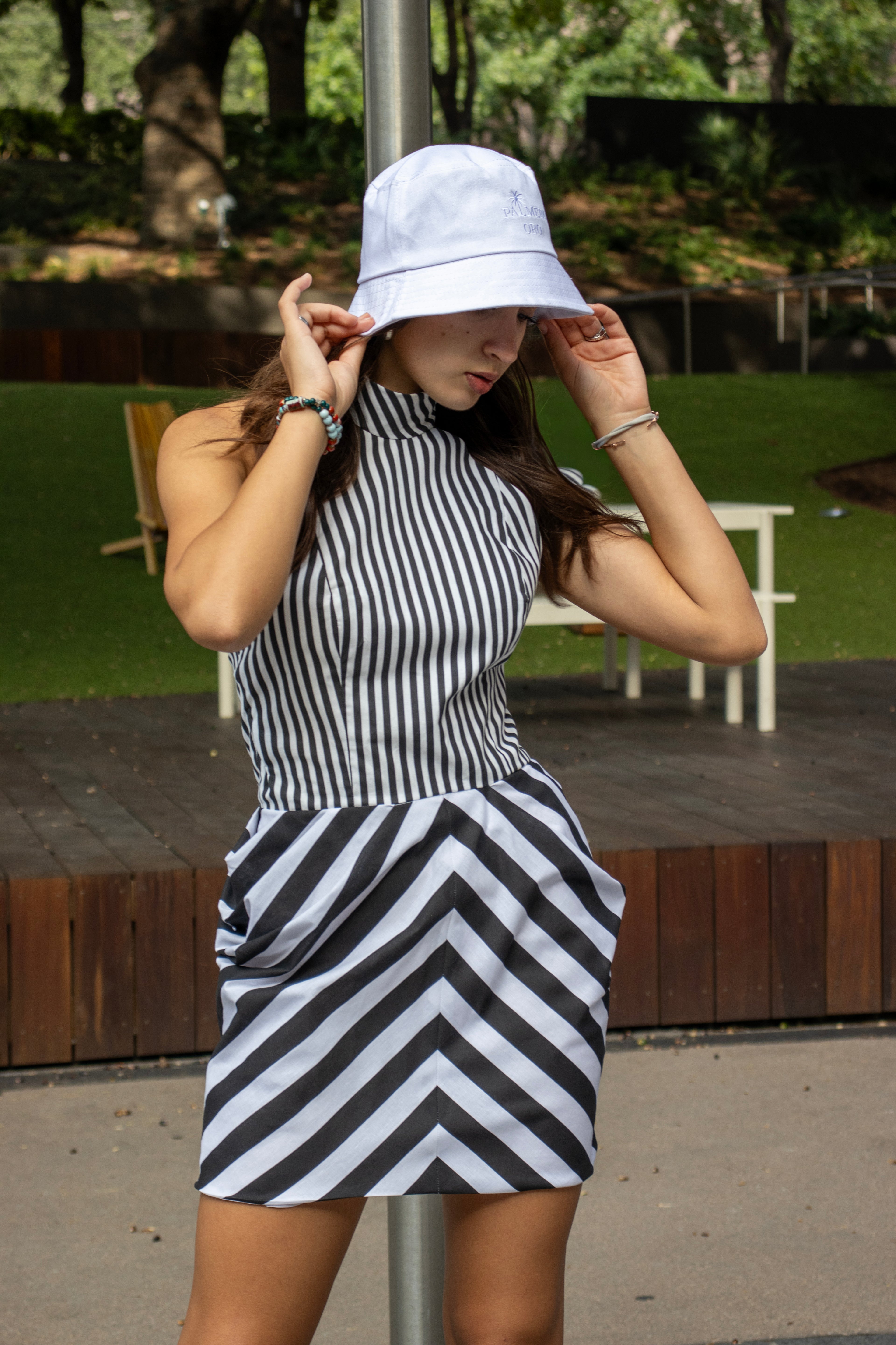 Woman wearing a black and white striped dress and white bucket hat outdoors.